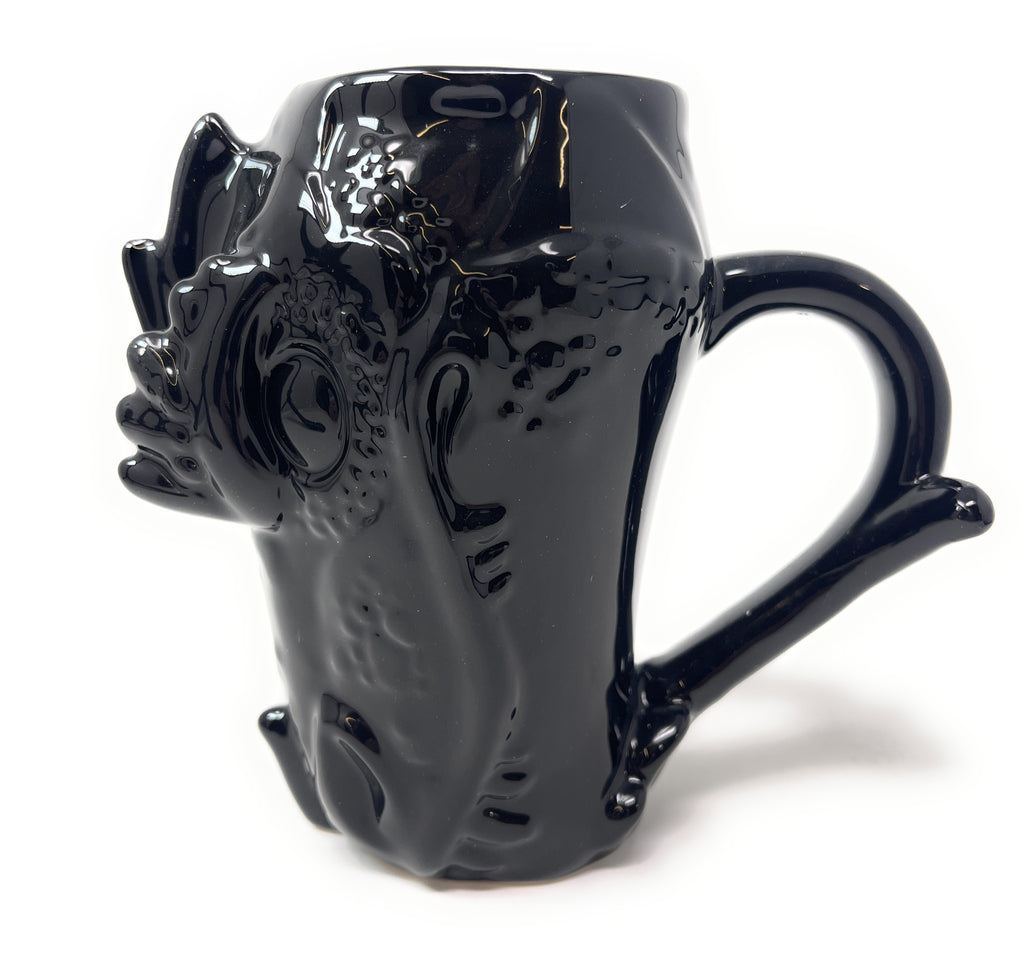 A glossy black ceramic mug shaped like a stylized animal face with a curved handle, photographed on a plain white background.
