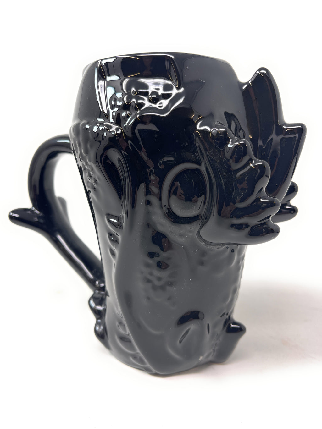 A glossy black ceramic mug shaped like a stylized creature or monster head, with a curved handle and sculpted details, photographed on a plain white background.