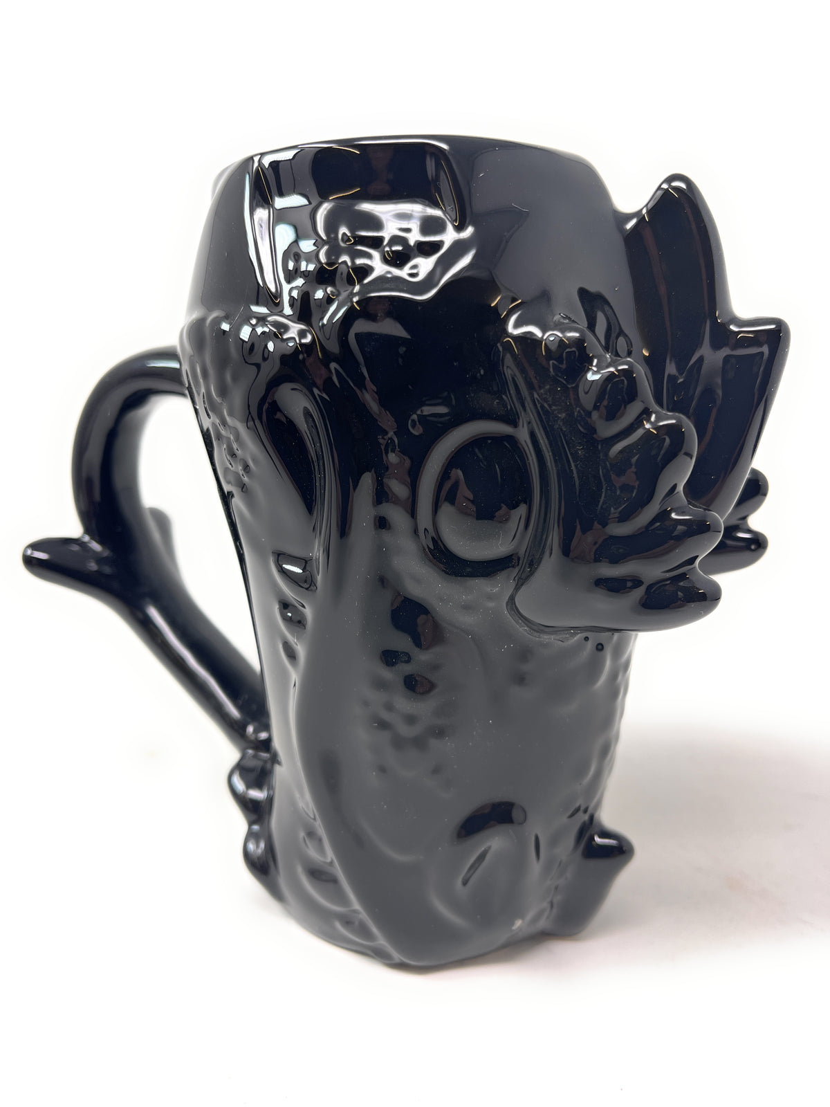 A glossy black ceramic mug shaped like a stylized creature or monster head, with a curved handle and sculpted details, photographed on a plain white background.