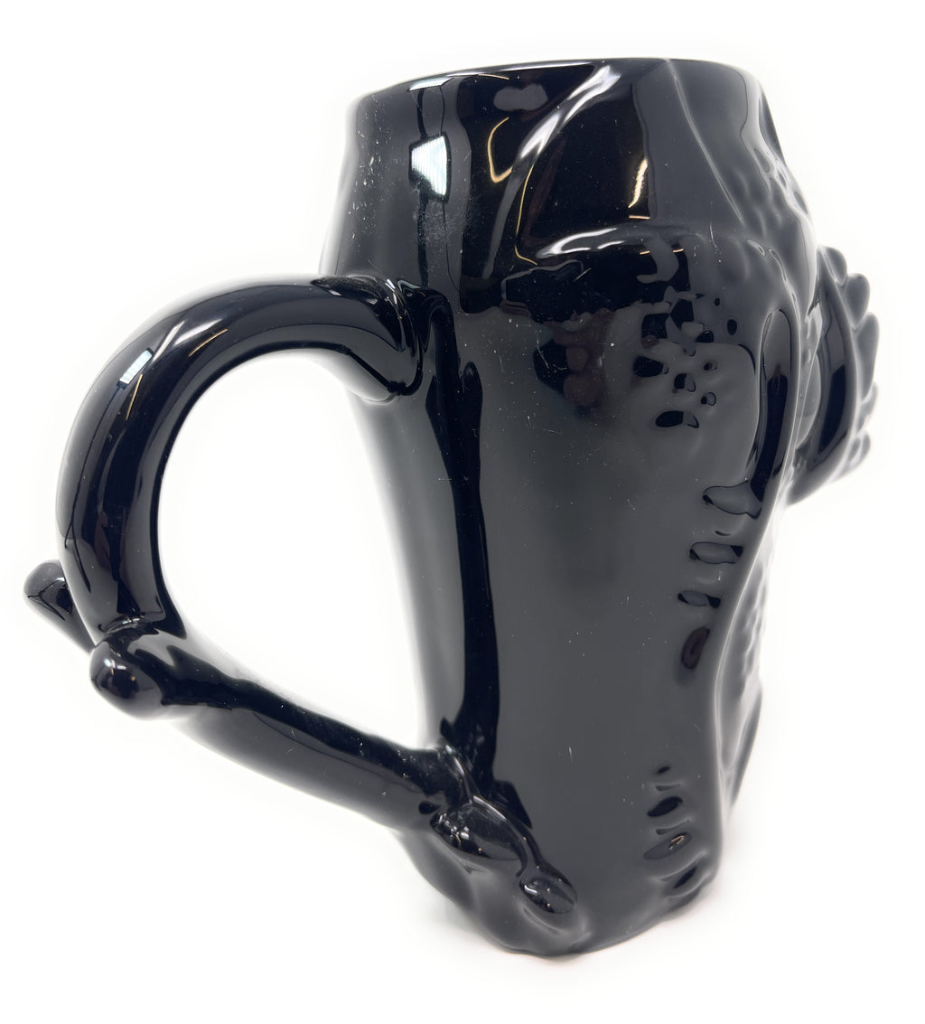 A glossy black ceramic mug shaped like a tree trunk, featuring a textured bark-like surface and a handle formed by branches.