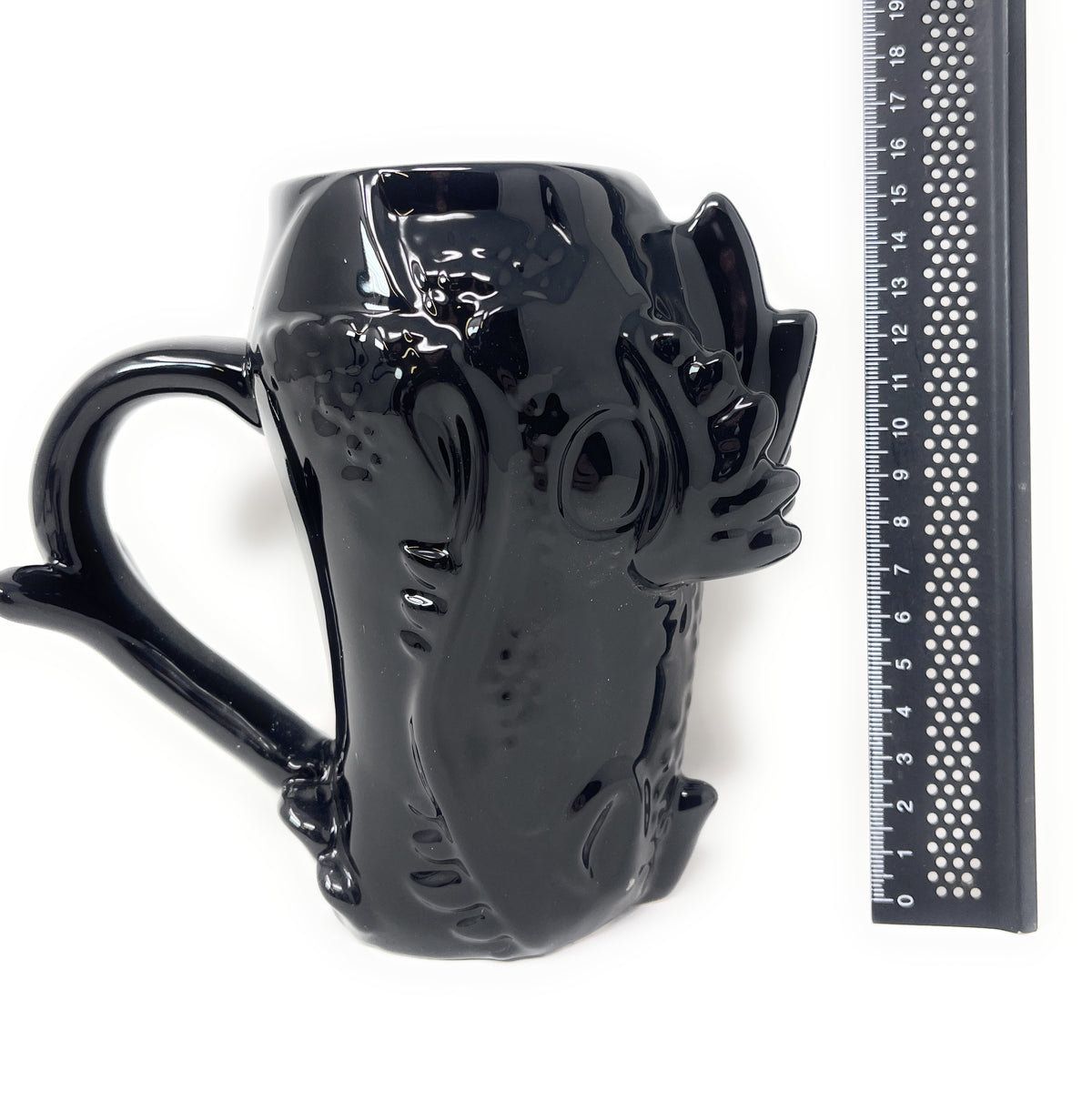 A glossy black ceramic mug shaped like a stylized creature or monster, shown on a white background next to a black ruler for scale.