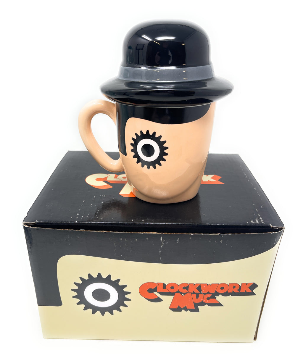 A novelty Clockwork Orange Ceramic Mug shaped like a stylized face wearing a black bowler hat, displayed on top of its black and beige branded retail box. The mug has a beige skin-toned face with a black gear-shaped eye and a glossy black hat.