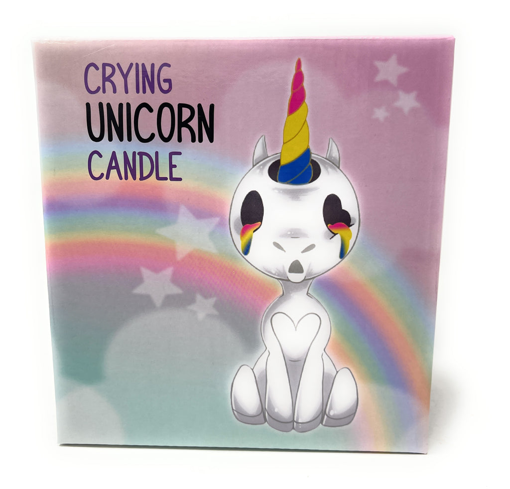 A square product box for a 'Crying Unicorn Candle' featuring a cute white cartoon unicorn with a rainbow horn, set against a pastel rainbow and starry background.