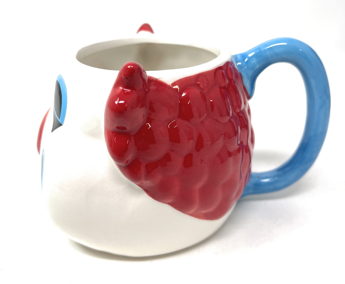 A ceramic mug with a glossy white body, a raised red clown face and body, and a blue handle, photographed on a white background.