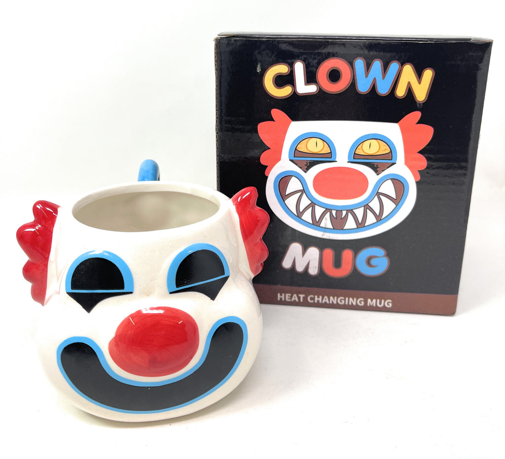 A novelty clown face heat-changing mug shown next to its black retail box. The mug is white with a red nose, red hair, blue outlines, and black facial features.